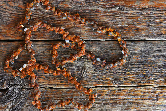 A top view image of a very old and rusted chainsaw chain on a dark wooden table top. 