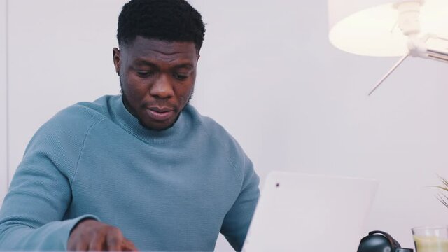 African American black man sitting at the table in front of a laptop and using a smartphone. Remote work concept. High quality 4k footage