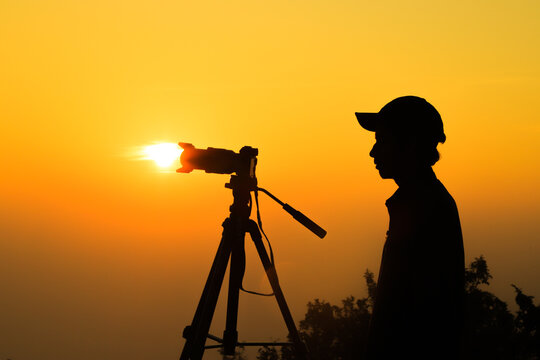 Silhouette of a young photographer, taking pictures of the landscape at sunset