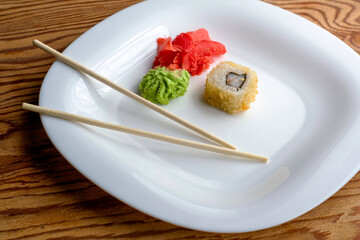 baked sushi with eel wasabi ginger and chopsticks on a white plate