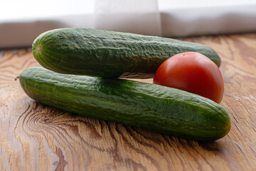 two cucumbers and one tomato on a wooden background