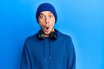 Hispanic young man wearing sweatshirt and headphones afraid and shocked with surprise expression, fear and excited face.
