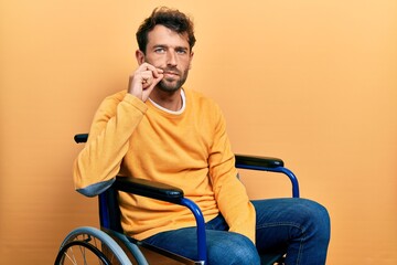 Handsome man with beard sitting on wheelchair mouth and lips shut as zip with fingers. secret and...