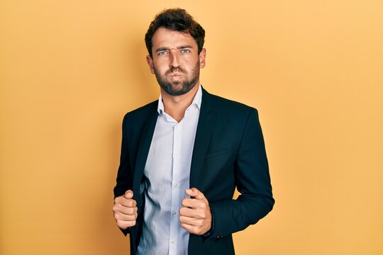 Handsome man with beard wearing business suit holding jacket puffing cheeks with funny face. mouth inflated with air, catching air.