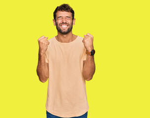 Handsome young man with beard wearing casual tshirt excited for success with arms raised and eyes closed celebrating victory smiling. winner concept.