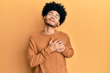 Fototapeta na wymiar Young african american man with afro hair wearing casual winter sweater smiling with hands on chest with closed eyes and grateful gesture on face. health concept.