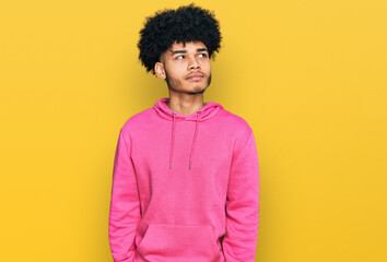 Obraz na płótnie Canvas Young african american man with afro hair wearing casual pink sweatshirt smiling looking to the side and staring away thinking.