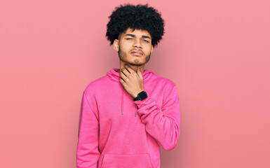 Fototapeta na wymiar Young african american man with afro hair wearing casual pink sweatshirt touching painful neck, sore throat for flu, clod and infection