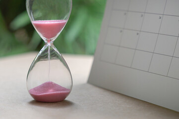 Hour glass with sand flowing,  next to calendar. Passing of time or deadline concept.