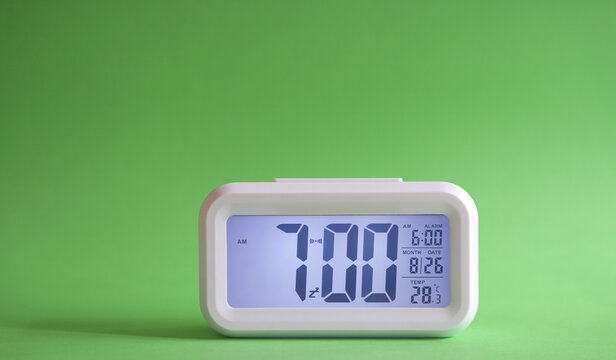 Digital alarm clock on table with green background. Copy space.