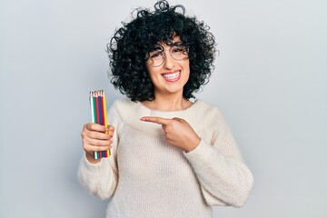 Young middle east woman holding colored pencils smiling happy pointing with hand and finger