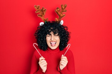 Young middle east woman wearing cute christmas reindeer horns sticking tongue out happy with funny expression.