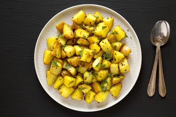 Homemade Roasted Potatoes with Mustard Seeds on a Plate on a black background, top view. Flat lay, overhead, from above.