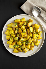 Homemade Roasted Potatoes with Mustard Seeds on a Plate on a black surface, top view. Flat lay, overhead, from above.