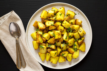 Homemade Roasted Potatoes with Mustard Seeds on a Plate on a black background, top view. Flat lay, overhead, from above.