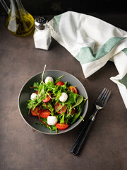 light snack. fresh green salad with lettuce leaves and arugula greens. with cherry tomatoes and mozzarella cheese. low key, dark mood, copy space. for menus and magazines with recipes