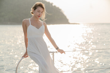 Woman wearing white dress relax on sailing yacht, romantic sunset.