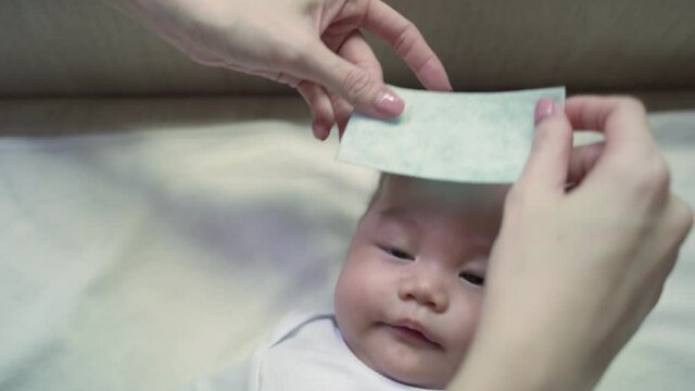 asian woman mother parent applying baby infant get fever and apply cool patch on forehead sleeping at home after vaccination. cold pad gel healing temperature. baby sick after back from hospital.