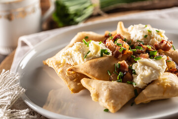 Fried pierogi served on a plate with bryndza cheese, bacon, and chives