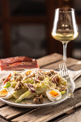 Caesar salad with boiled eggs, bacon, and croutons served on a plate next to a glass of white wine