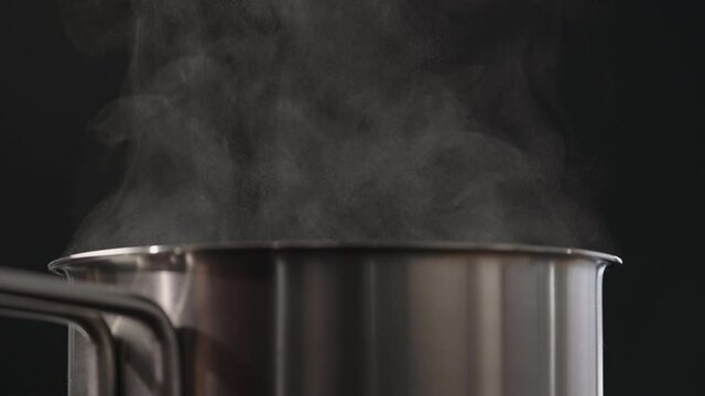 Slow motion man hand stiring with fork in saucepan with rising steam