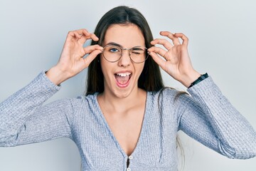 Young brunette teenager wearing glasses winking looking at the camera with sexy expression,...