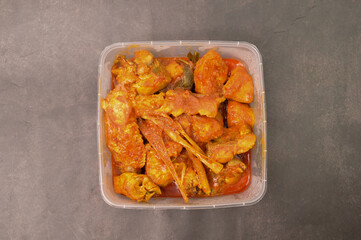 Hot spicy chicken in a plastic box over black background