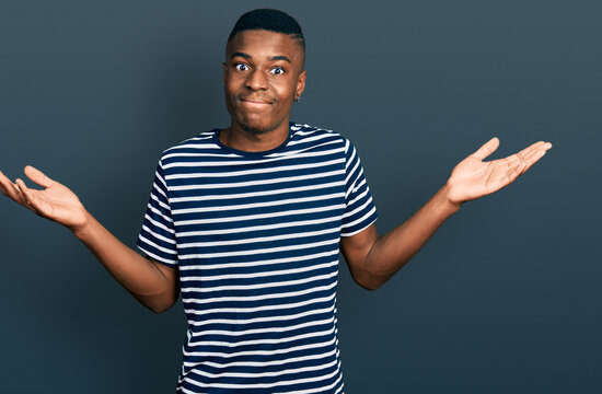 Young african american man wearing casual striped t shirt clueless and confused with open arms, no idea and doubtful face.