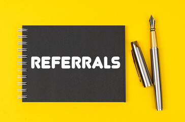 On a yellow background lies a pen and a black notebook with the inscription - Referrals