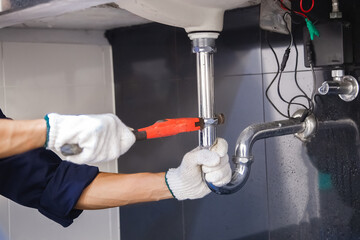 Plumber fixing white sink pipe with adjustable wrench.