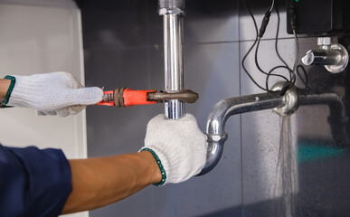 Plumber fixing white sink pipe with adjustable wrench.