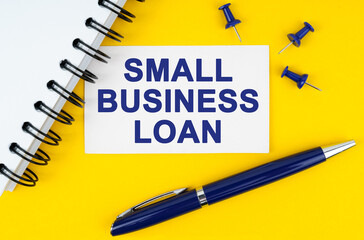 On a yellow background lies a notebook, a pen and a business card with the inscription - SMALL BUSINESS LOAN