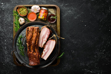 Smoked bacon with spices. Piece of smoked meat on a black stone background. Top view.