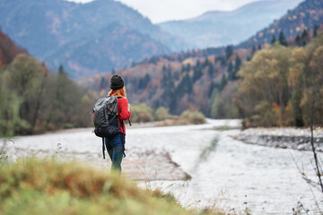 woman in a red sweater with a backpack in the mountains on nature near the river pond lake