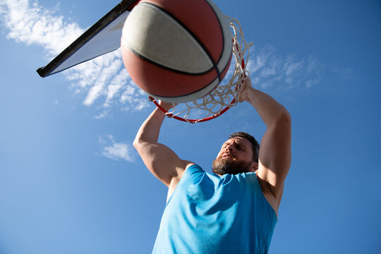 Close up image of professional basketball player making slam dunk during basketball game in outdoor basketball court.