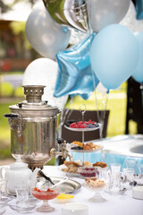 Tea drinking with a Russian samovar, jam, sweets and delicious berries. Unusual table setting for a holiday. Outdoor birthday party.