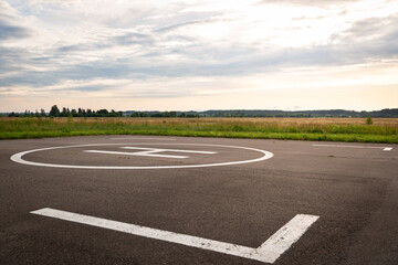 View of the private helipad on a warm summer evening. An asphalt helipad against the backdrop of a green field and a cloudy evening sky.