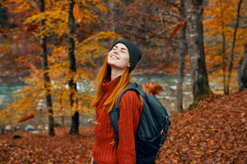 Fototapeta na wymiar woman in a hat with a backpack and a sweater is resting in the autumn forest near the river in nature