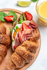 sandwiches Croissant with avocado, asparagus, jamon, ham, prosciutto, strawberries, sunny side up eggs and juice, Food recipe background. vertical image