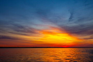 Obraz premium A fiery sunset on a navigable river in the distance port cranes can be seen