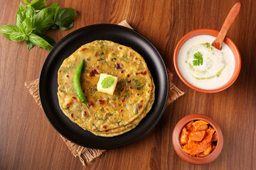 Palak paratha butter on spinach paratha , parantha ,chapati Indian flatbread roti made from spinach served in golden plate with yogurt mint dip, mango pickle, North Indian breakfast food Delhi India.