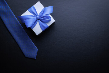 Father day gift. White box with bow ribbon, blue bowtie or tie on dark background. Concept of Fathers Day greeting card, copy space for text.