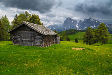 Fototapeta na wymiar Cloudy alpine scenery with wooden hut and snowy mountains, Dolomites