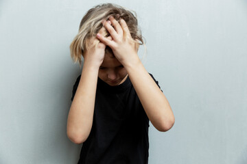 The boy in horror is holding his head with his hands. Gray background. Stress and oppression.