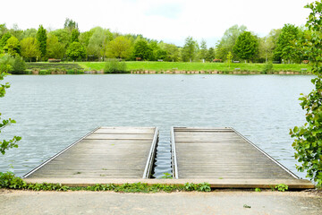 View of a double wooden pontoon by a lake in summer. Lush vegetation in the background.