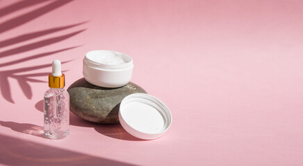 hand cream jar on the stone and dropper bottle of serum hyaluronic acid collagen  with natural sunlight effect copy space on pink background