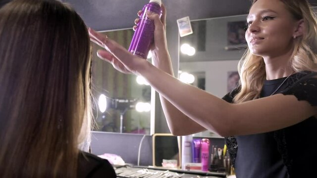 Hairdresser spraying hairspay on hairstyle of beautiful lady at beauty shop or barbershop. Woman uses spray can to fixate hairdo at cosmetic salon in front of mirror. beauty industry, self-care