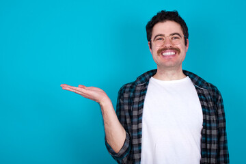Positive glad young Caucasian man with moustache wearing plaid shirt against  says: wow how exciting it is, has amazed expression, shows something on blank space with open hand. Advertisement concept.