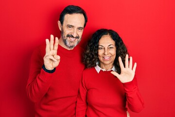 Middle age couple of hispanic woman and man hugging and standing together showing and pointing up with fingers number eight while smiling confident and happy.