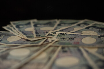 Blurred focus of pile of Japanese money in 1000 yen bills and 10000 yen bills on black background in soft focus